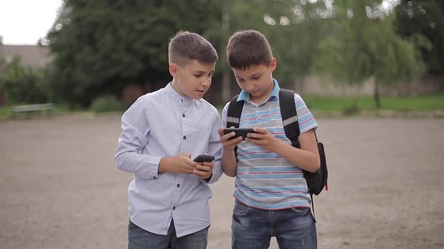 Two boys plays online games after school classes. Young boys smile and use phone
