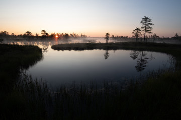 Fototapeta na wymiar Sunrise over lake with sun star and tree silhouettes