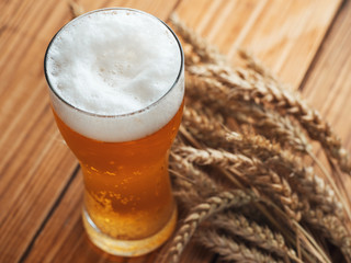 A glass of cold beer close-up and ears of wheat on a wooden table