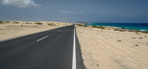 Fototapeta na wymiar Natural landscape with amazing dunes and asphalt road in Fuerteventura, Natural park Corralejo, Canary Island Spain. Summer exotic vacation postcard from a tropical island in the ocean. Panorama view