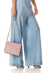 woman wearing summer high heeled sandals in polka-dot blue pants and pink woman handbag on white background.