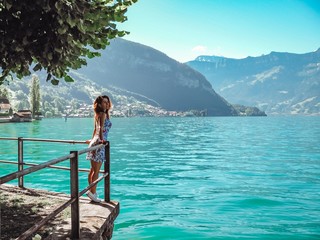 Brunette girl with long hair in a blue dress stands on the waterfront of the city of Thun, lake Geneva, transparent turquoise