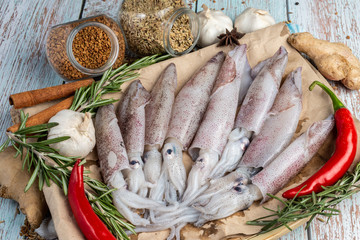 Fresh Raw Squids surrounded by spices and ingredient on a wooden table
