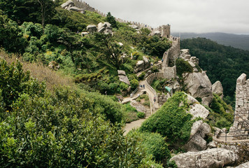 Fototapeta premium Green hills and stone towers of the 8th century The Moorish Castle over town Sintra. Historical landscape in Portugal and a UNESCO world heritage site