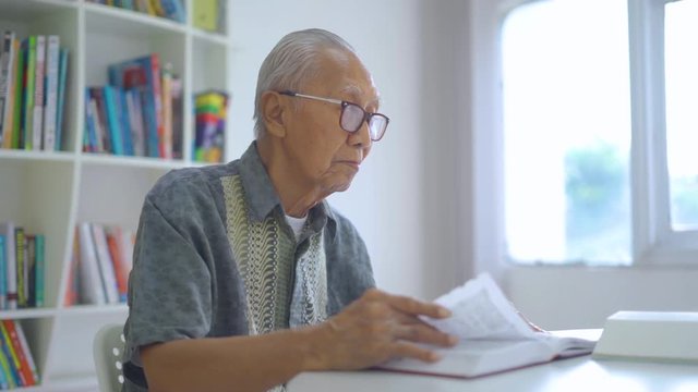 Senior man reading books while wearing glasses on the table in the library. Shot in 4k resolution