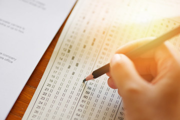 Obraz premium take the exam final high school hand student holding pencil writing on paper answer sheet - education college in class taking notes sitting learning writing selected choice in examination room