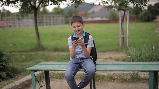 Young boy with backpack sitting on the bench and play online games during school break