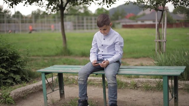 Handome young boy sitting on the bench and play online games during school break