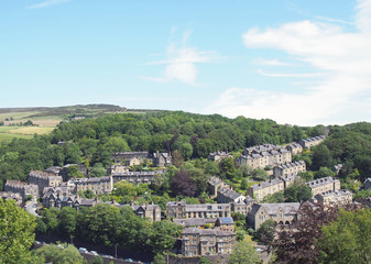 Fototapeta na wymiar a scenic aerial view of the town of hebden bridge in west yorkshire with streets of stone houses and roads between trees and a blue summer cloudy sky
