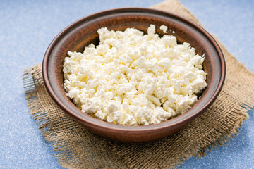 Homemade cottage cheese in a bowl on a sack and on a blue table. top view.