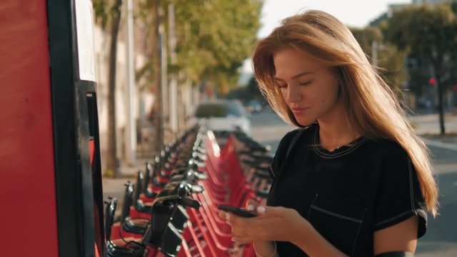 Row of red bicycles in a bike rack, available for rental on the streets of Barcelona, girl take bike with card phone application