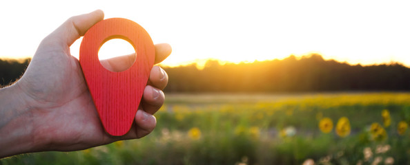 A hand is holding a red location marker in the sunset background. The concept of tourism and...