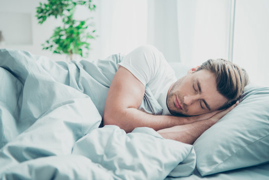 Portrait of cute blonde-haired man lying in bed close eyes indoors room