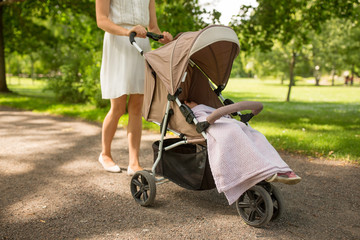 family, motherhood and people concept - mother with child sleeping in stroller walking at summer...