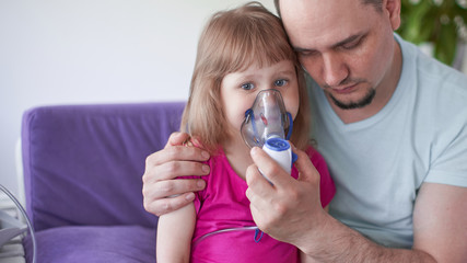 father and daughter do inhalations. caring dad helps her daughter breathe through the mask