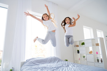 Low angle photo of cheerful kids jumping bed have free time raise hands feel content room indoors...