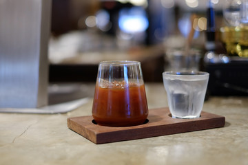 A beautiful ice black coffee served with glass of drinking water on wooden coaster. Selective focus. blur background