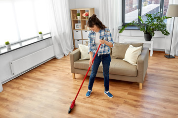cleaning housework and housekeeping concept - happy asian woman with broom sweeping floor at home