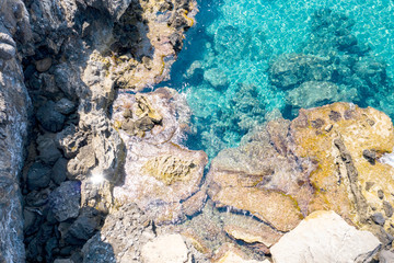 Aerial view of turquoise sea water and rocks by the seashore.