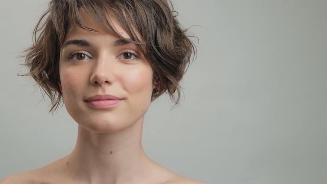 Attractive young woman with natural skin making silence gesture while looking at the camera over grey background isolated