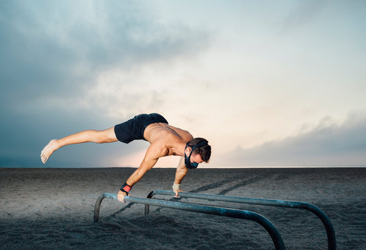 fitness, sport, training, calisthenics and lifestyle concept - Young man training on parallel bars on the street