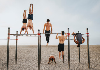 fitness, sport, training, calisthenics and lifestyle concept - Group of guys training on the beach workout bars - obrazy, fototapety, plakaty