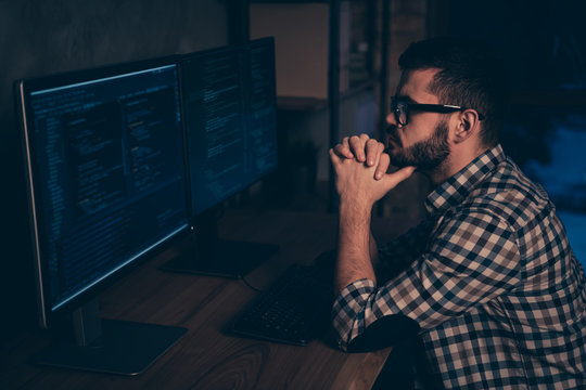 Close up side profile photo handsome he him his guy ponder pensive hands arms chin coder code development outsource IT processing two monitors table office wear specs formalwear plaid shirt