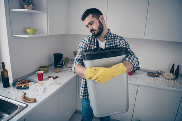 Portrait of his he nice attractive serious focused sad bored tired bearded guy wearing checked shirt doing domestic mess chaos in modern light white interior style kitchen indoors
