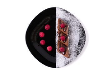 Chocolate pancakes stuffed with cottage cheese decorated with raspberries and powdered sugar. Top view