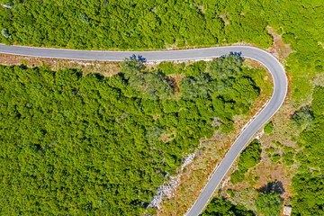 Aerial view of road in high mountains among green trees.