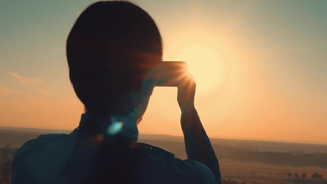 woman holding smartphone taking pictures of the sky at sunrise