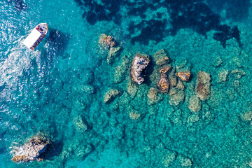 Naklejka na ściany i meble Aerial view of turquoise sea water and rocks by the seashore.