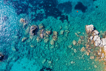 Aerial view of turquoise sea water and rocks by the seashore.