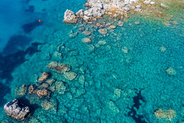 Aerial view of turquoise sea water and rocks by the seashore.
