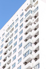Building construction and architecture. The facade of a new high-rise bright house with balconies and windows against a blue sky