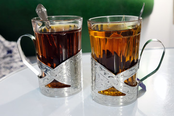 Two cups of tea in metal coasters stand on a white table. tea glass holder on the table in the train
