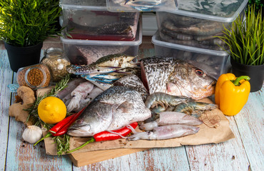 Fresh Seafood - Golden Snapper, Sea Bass, Prawns, Crabs, and Squids - on a wooden table surrounded by raw ingredients.