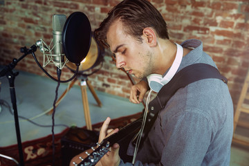 Young man in headphones recording music video blog home lesson, playing guitar or making broadcast...