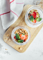 Two jars with tasty parfaits made of granola, strawberries and yogurt on white marble table, top view