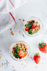 Two jars with tasty parfaits made of granola, strawberries and yogurt on white marble table, top view