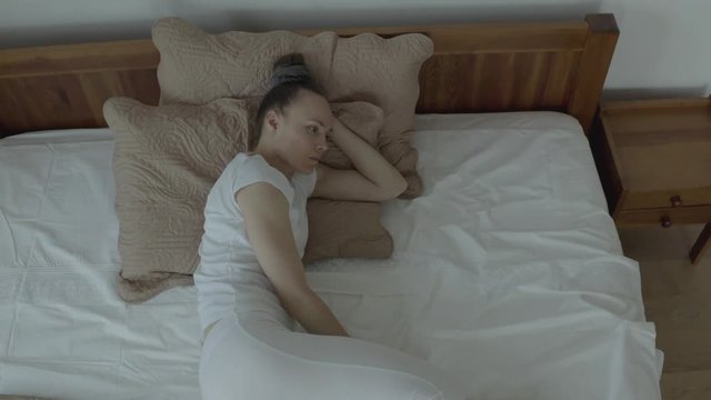 Reflective young woman between 30 and 35 years old stays in her bed.
