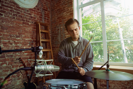 Young man recording music video blog, home lesson or song, playing drums or making broadcast internet tutorial while sitting in loft workplace or at home. Concept of hobby, music, art and creation.