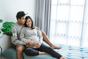 happiness husband and wife feel pregnancy, sit back together on the couch while holding the belly...