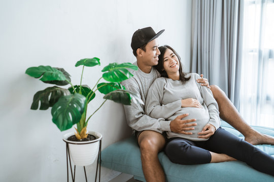 pregnant wife leaning in the husband's arms while relaxing sitting on the couch
