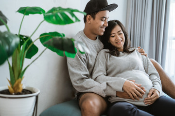 happiness couples feel the pregnancy, holding the wife's pregnant stomach, sitting on the couch beside the ornamental plants
