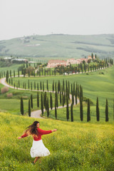 Young happy woman in red sweater and white skirt on background on spring Tuscany landscape. Dancing...