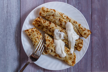 Homemade pancakes stuffed on a white plate, which stands on a wooden table.