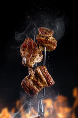Fork with pieces of delicious barbecued meat on black background