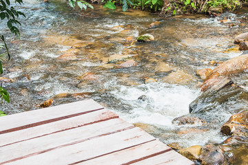 The scenery of the waterfall with water running through the rock near the wooden terrace.