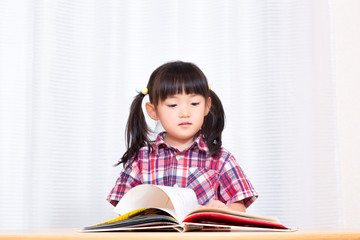 白背景の前で真剣に絵本を読む幼い女の子。幼児、教育、読書、学習、成長、育児イメージ